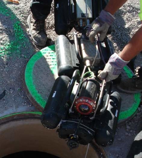 Gloved hands hold the Profiler robot over an open manhole in preparation for MSI