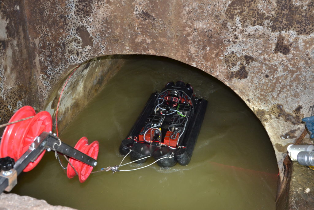 An inspection robot on floats is winched into a pipe half full of water