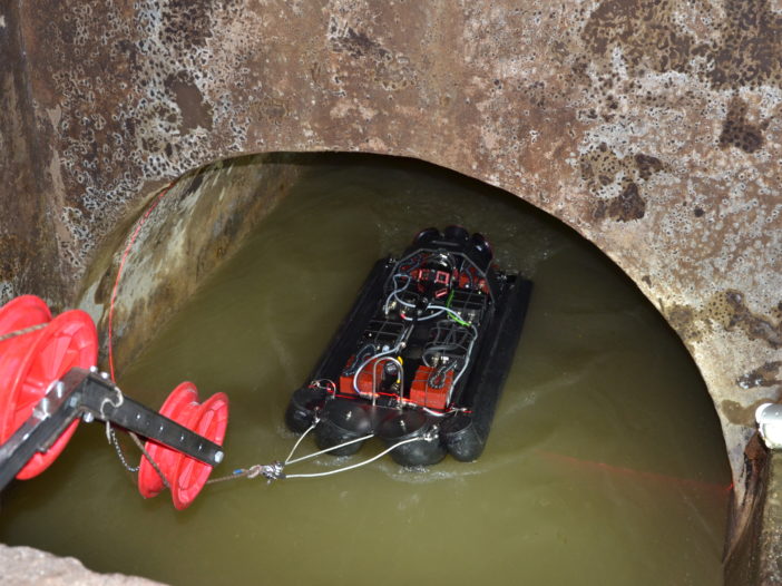 An inspection robot on floats is winched into a pipe half full of water