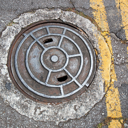 Manhole on a roadway with yellow double lines to the right of the mahole