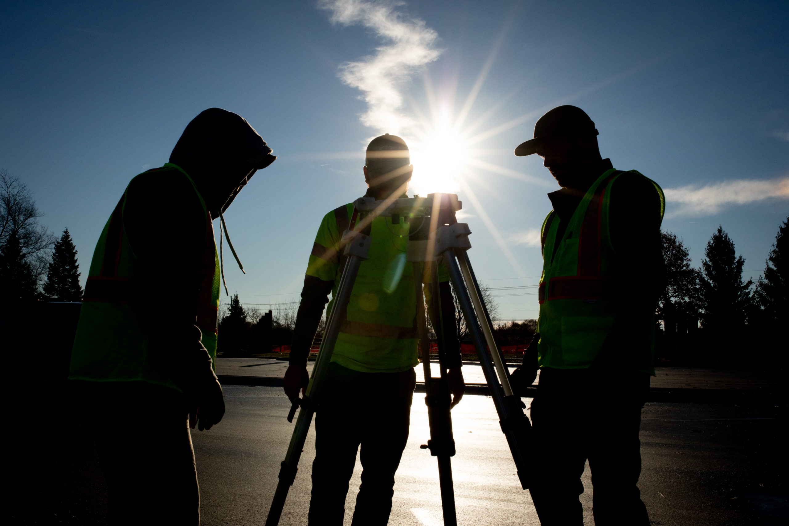 Shadowed image of three field crew members setting up the Vertue tripod with the sun in the background